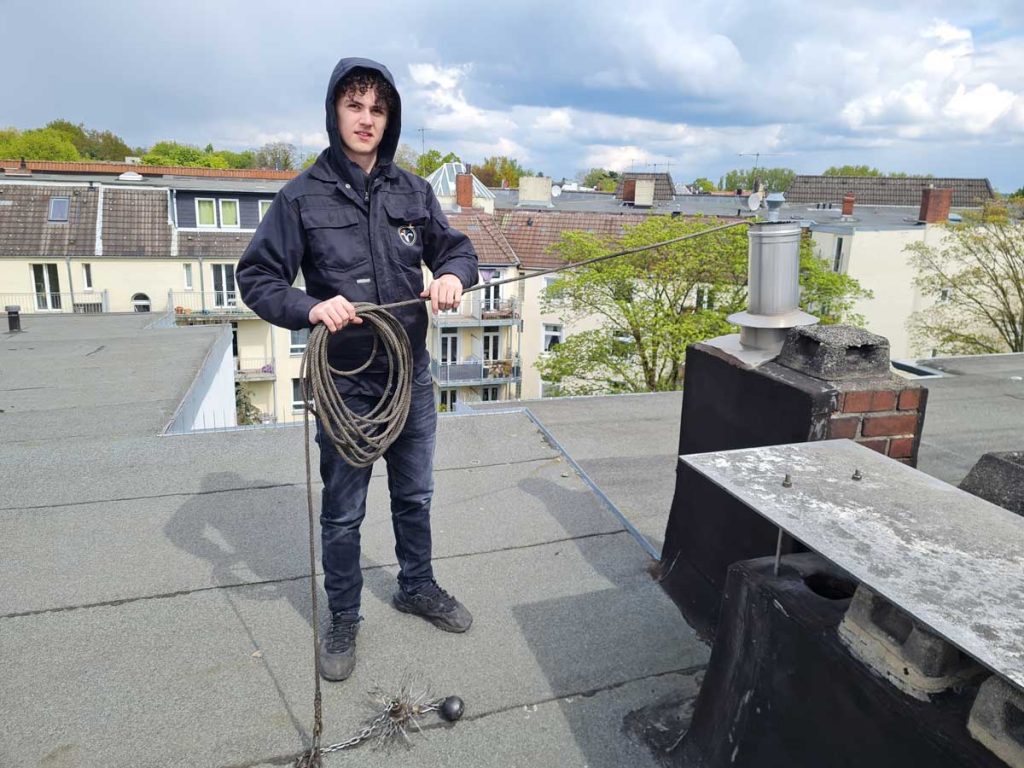 Praktikant beim Schornstein fegen auf dem Dach.