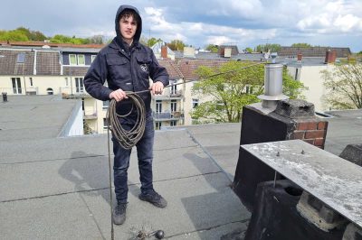 Praktikant beim Schornstein fegen auf dem Dach.